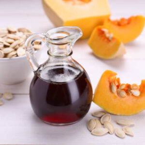 Fresh pumpkin seed oil in glass jug on white wooden table